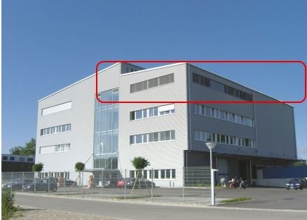 A multi-story office building with a modern, glass and concrete design. The building has several floors and a parking area in front of it.