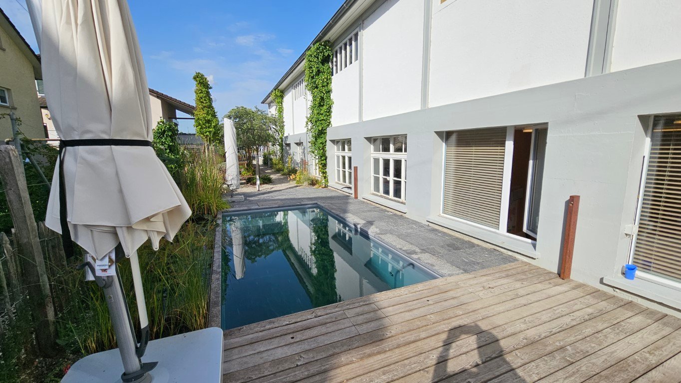 white-walled building, swimming pool, deck, closed umbrella, clear blue sky