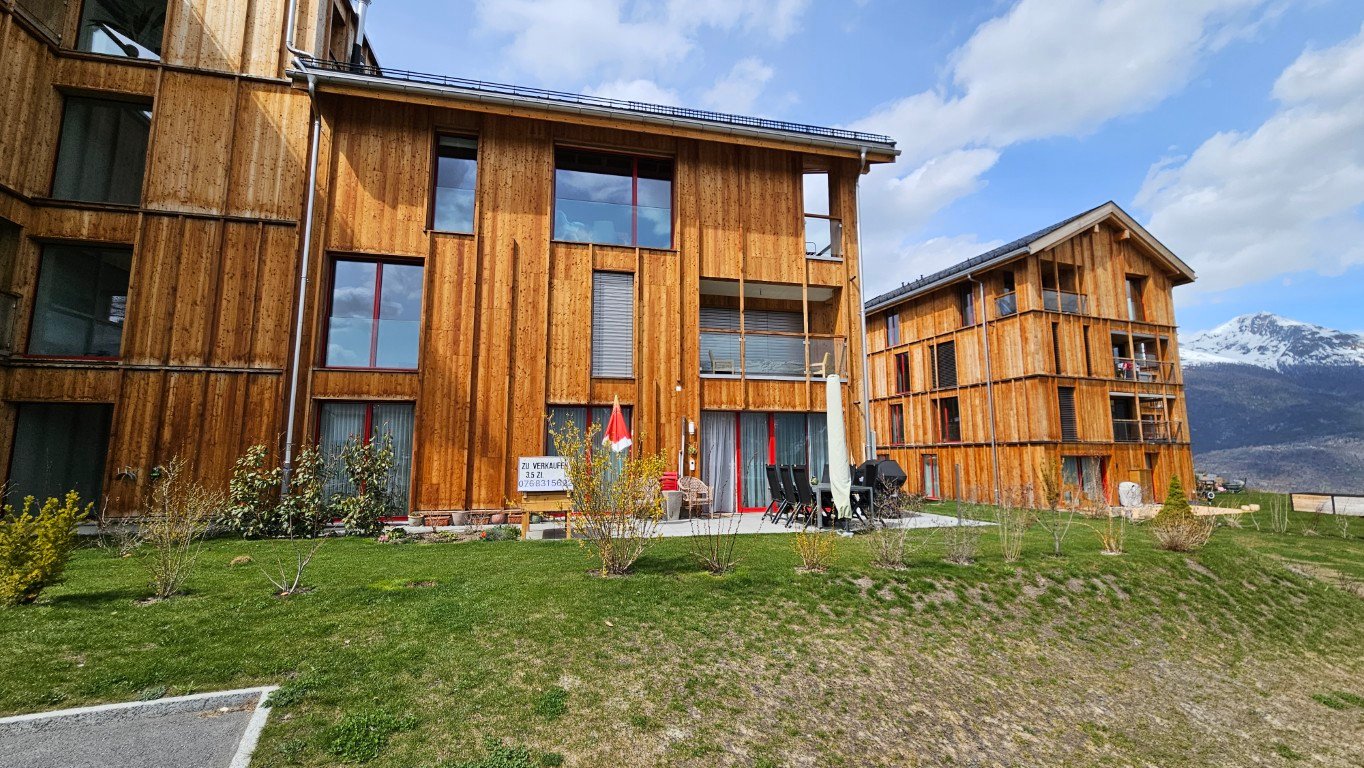 wooden exterior, large windows, balconies, outdoor seating area, green lawn, mountain view