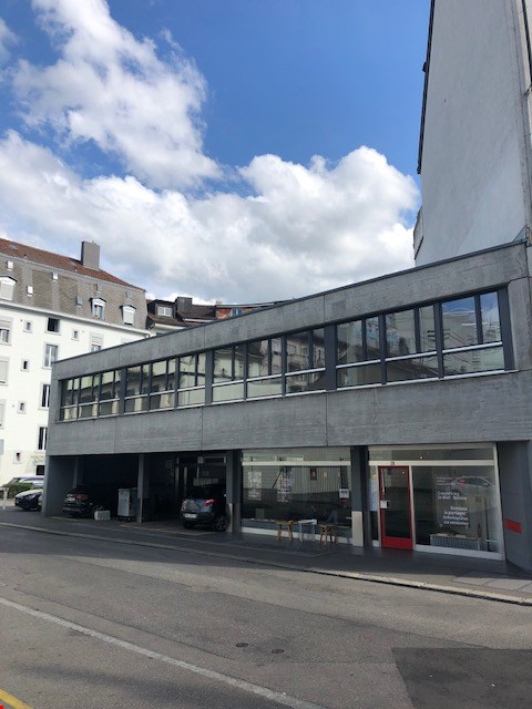 2 story building with large windows, car park in front, cars parked inside