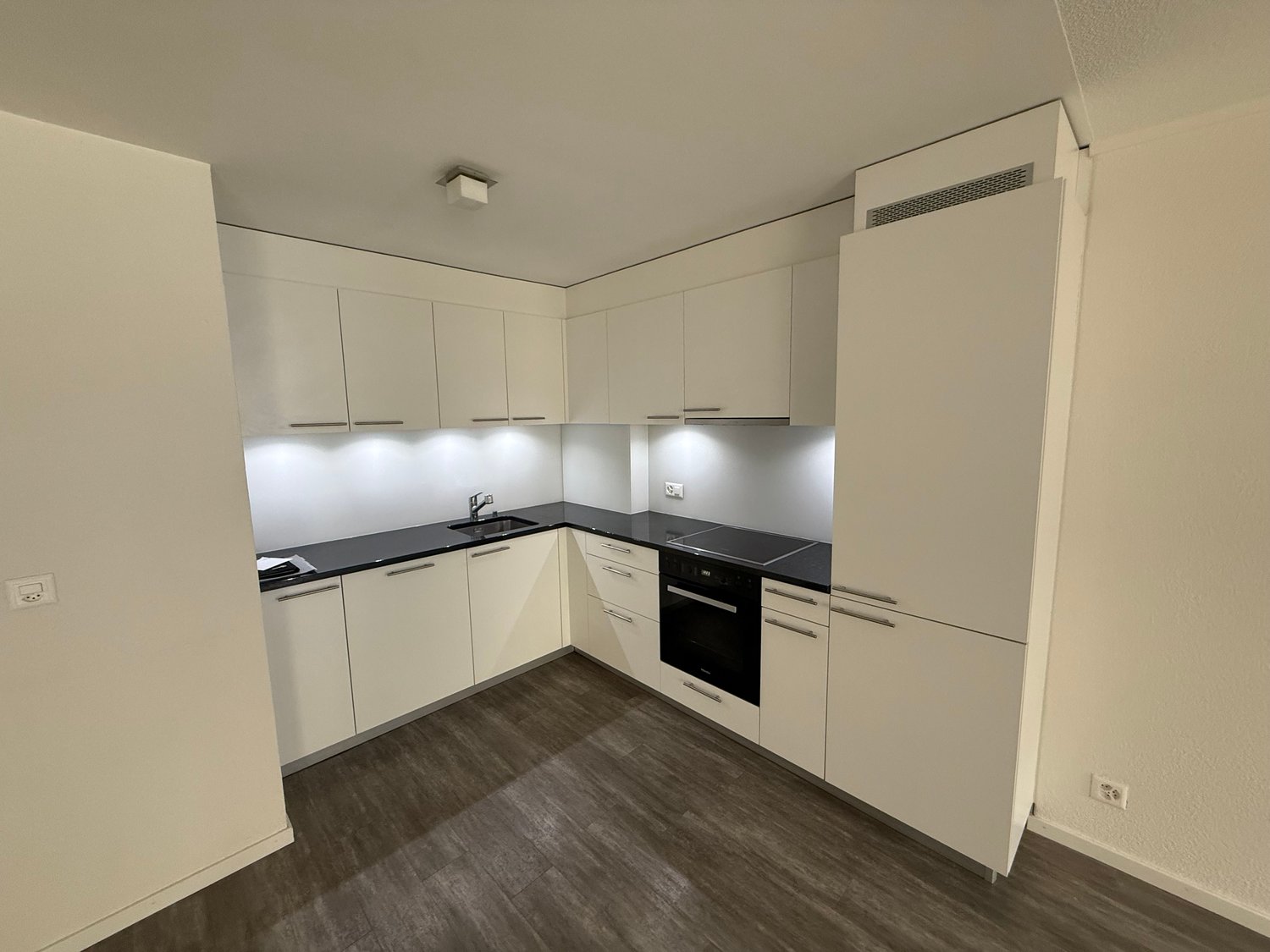 modern kitchen with white cabinets, black countertops, built-in oven and dishwasher, sink with faucet, wooden floor