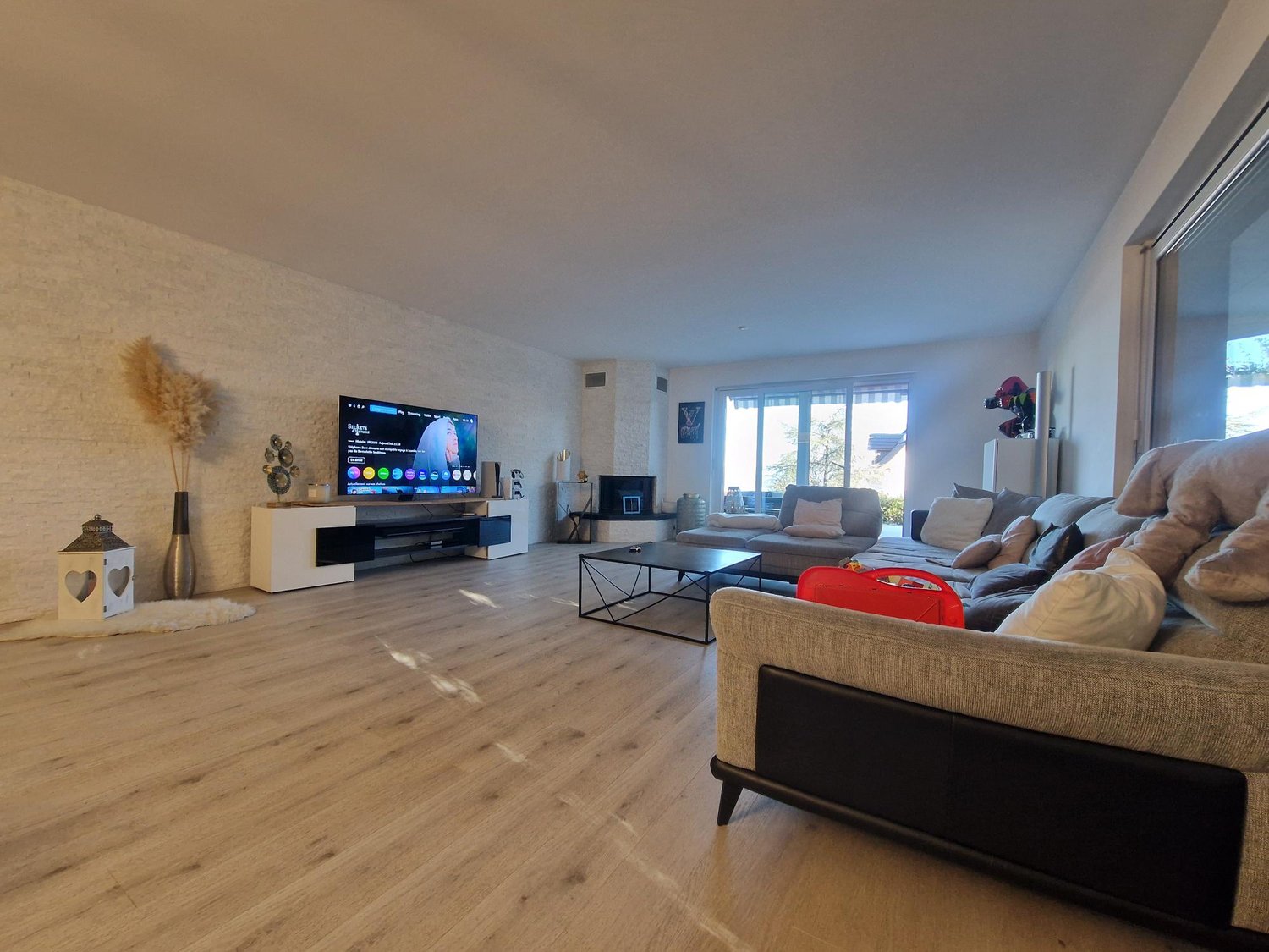 Living room with a large sofa, coffee table, TV, and a glass door leading to a balcony