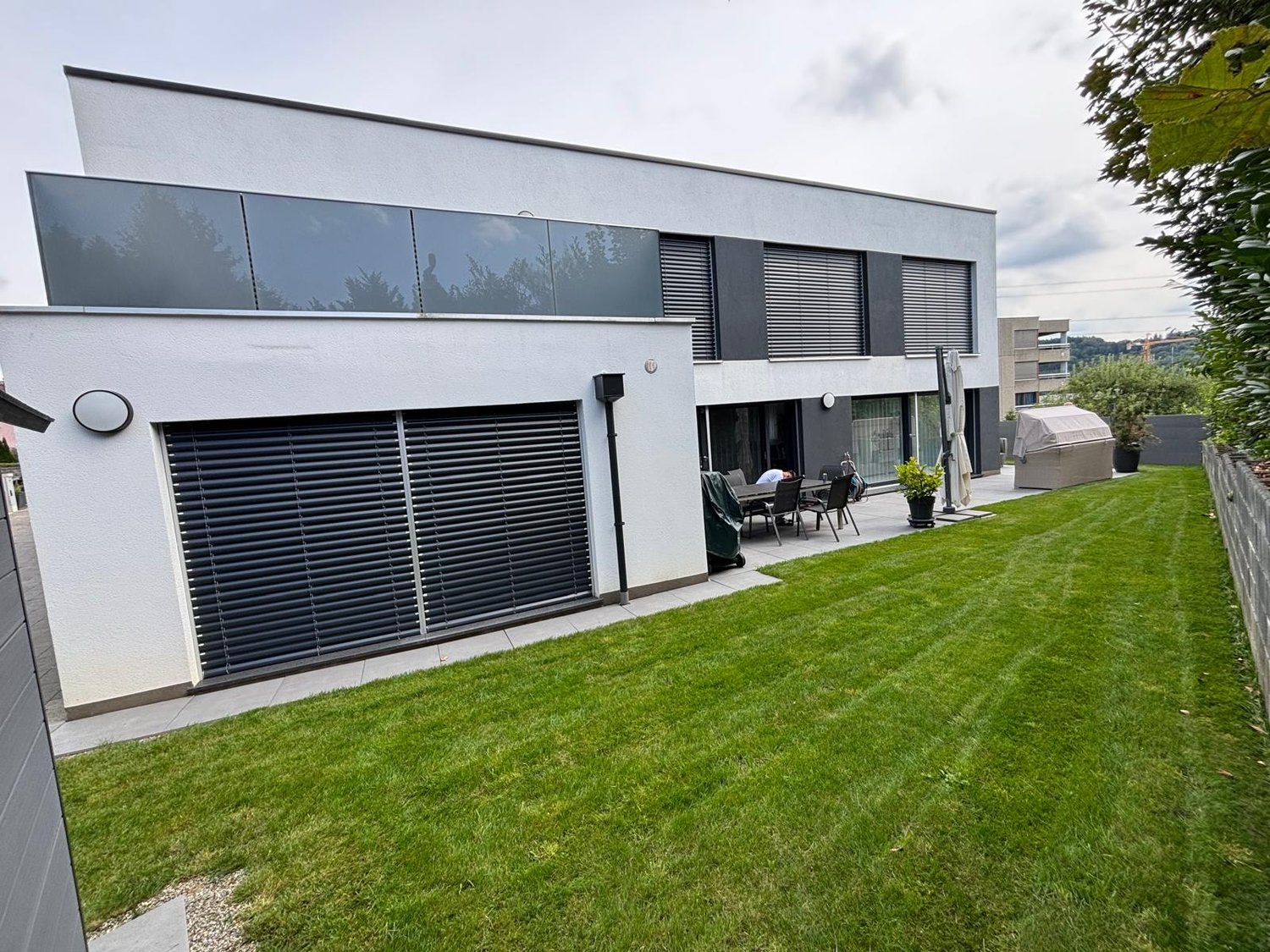 Modern white house, large garage, paved terrace, garden, glass windows, well-maintained green lawn