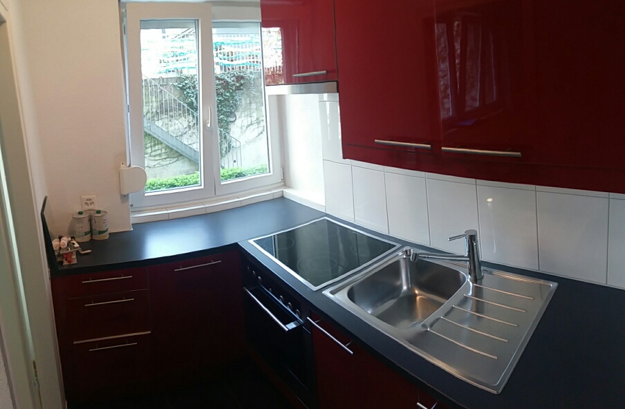 modern kitchen with red cabinets, black countertops, stainless steel sink, dishwasher, window