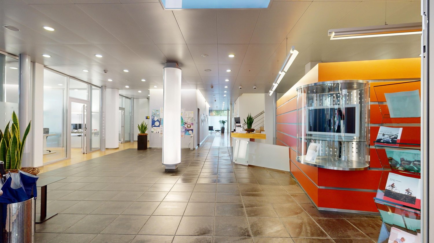 spacious lobby, light grey floor tiles, tall glass walls, white and orange walls, metal column, plants