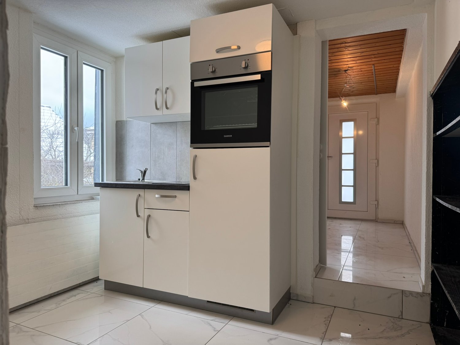 modern kitchen with white cabinets, black countertop, built-in oven, sink, and faucet, white tiled floor, window with view
