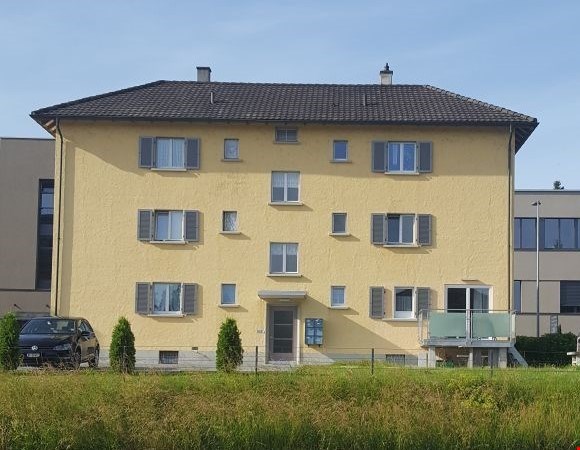 3 story yellow building, multiple windows, balcony, car parked in front