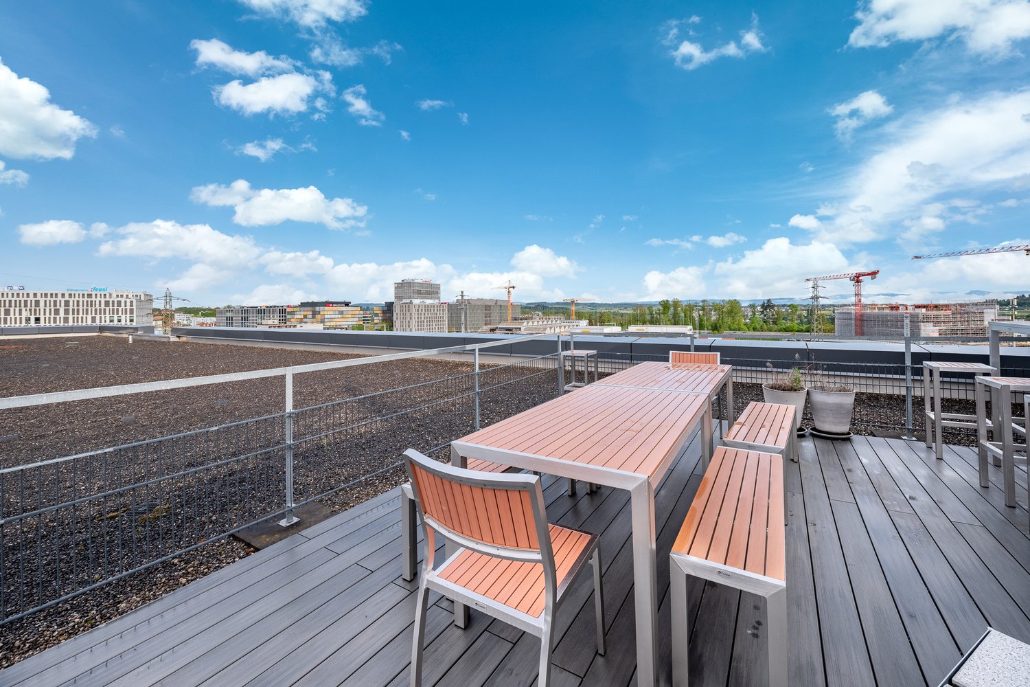 Outdoor wooden deck, dining table and chairs, metal railings, plants in pots, city skyline view
