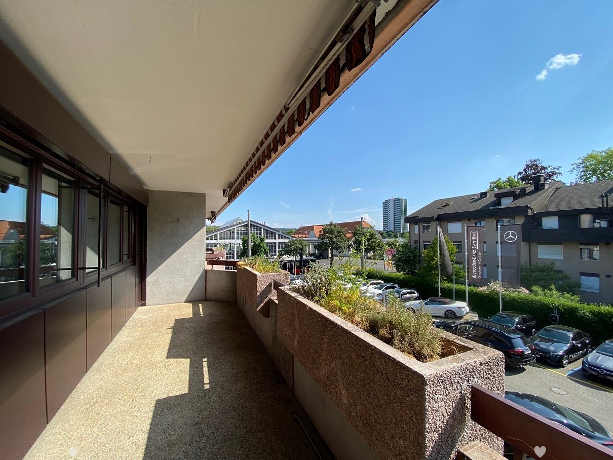 elevated balcony with large planter, railings, cars parked in lot below