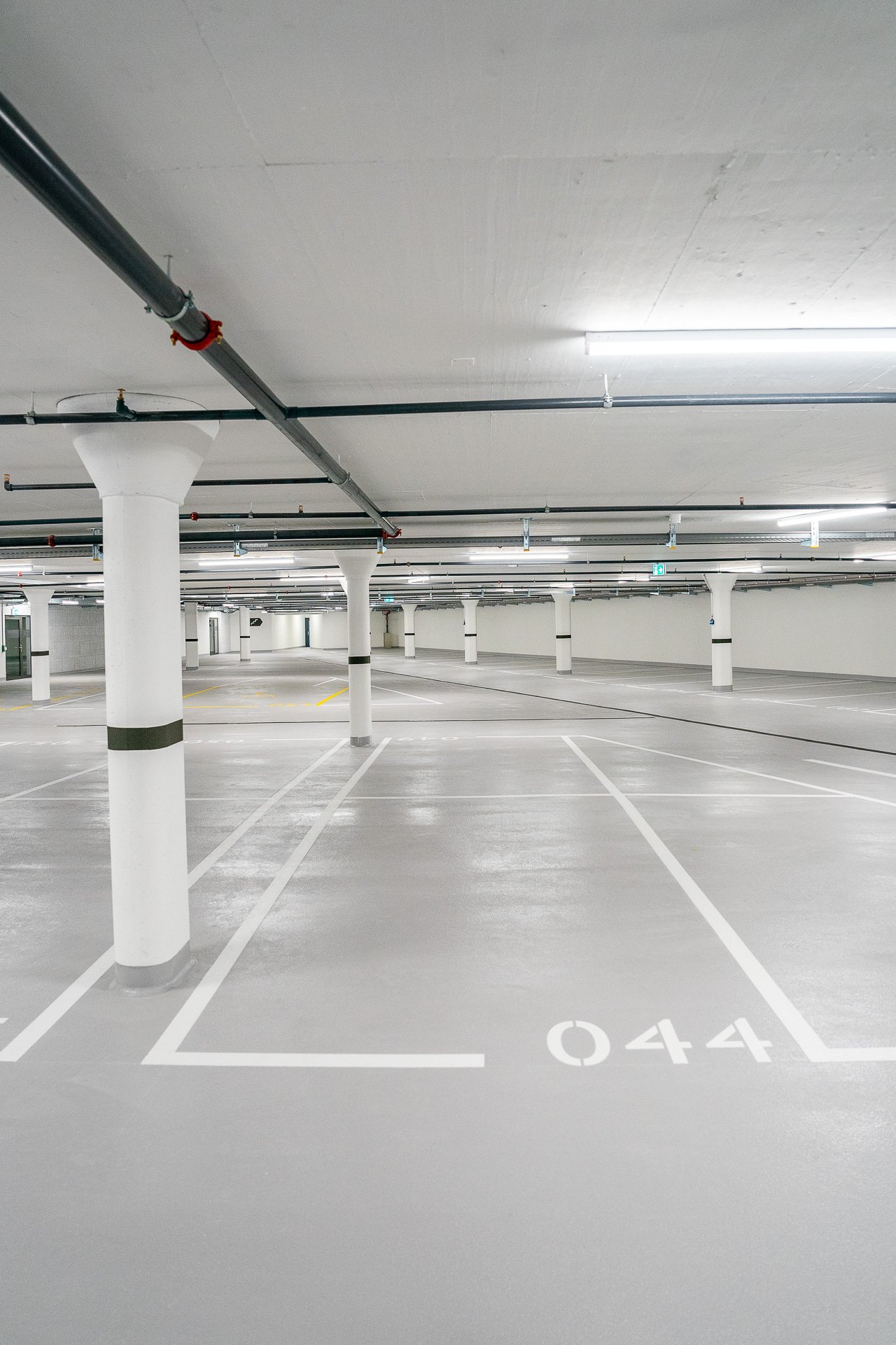 wide parking area, multiple columns, painted white lines, yellow markings, several pipes