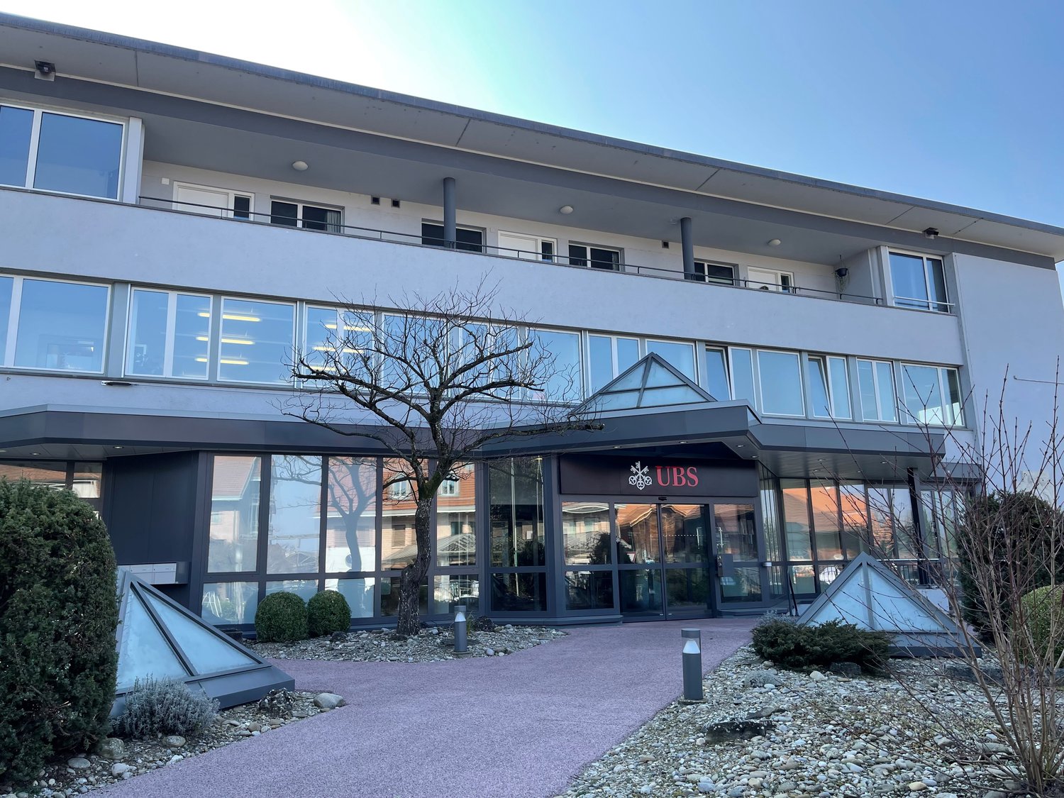 2-story commercial building with large glass windows, UBS bank signage, and a paved parking area in front