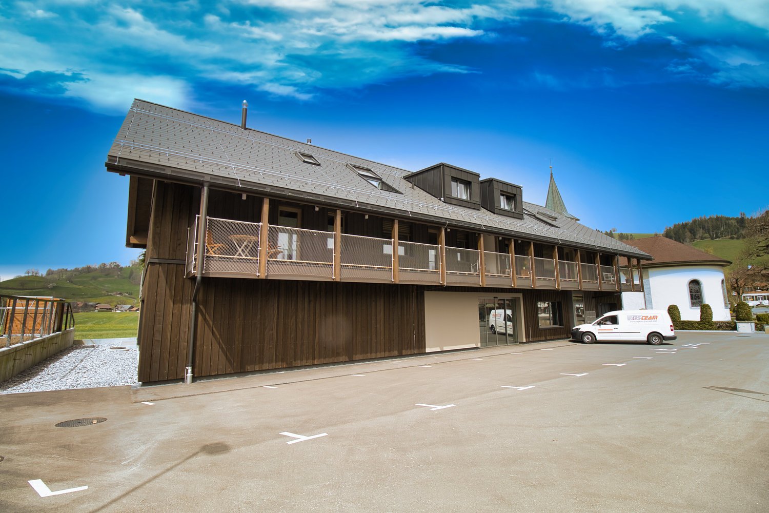 wooden exterior, gray roof, balcony, parking area, white van