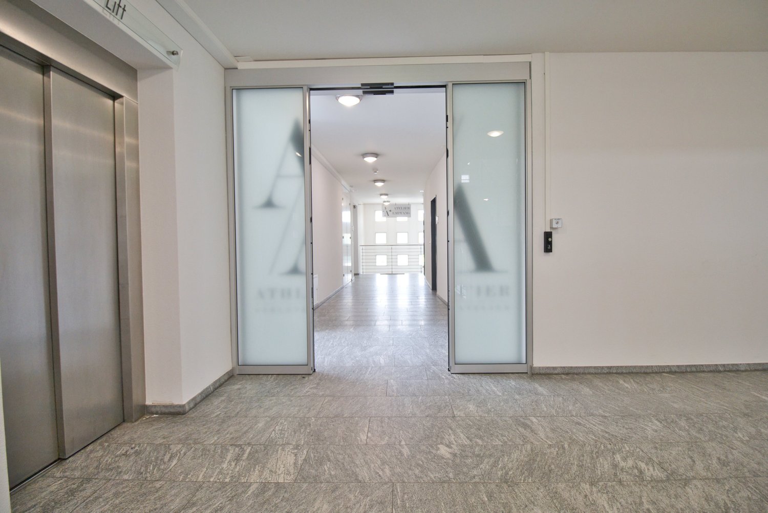 Empty hallway with gray tiles, glass doors, and ceiling lights