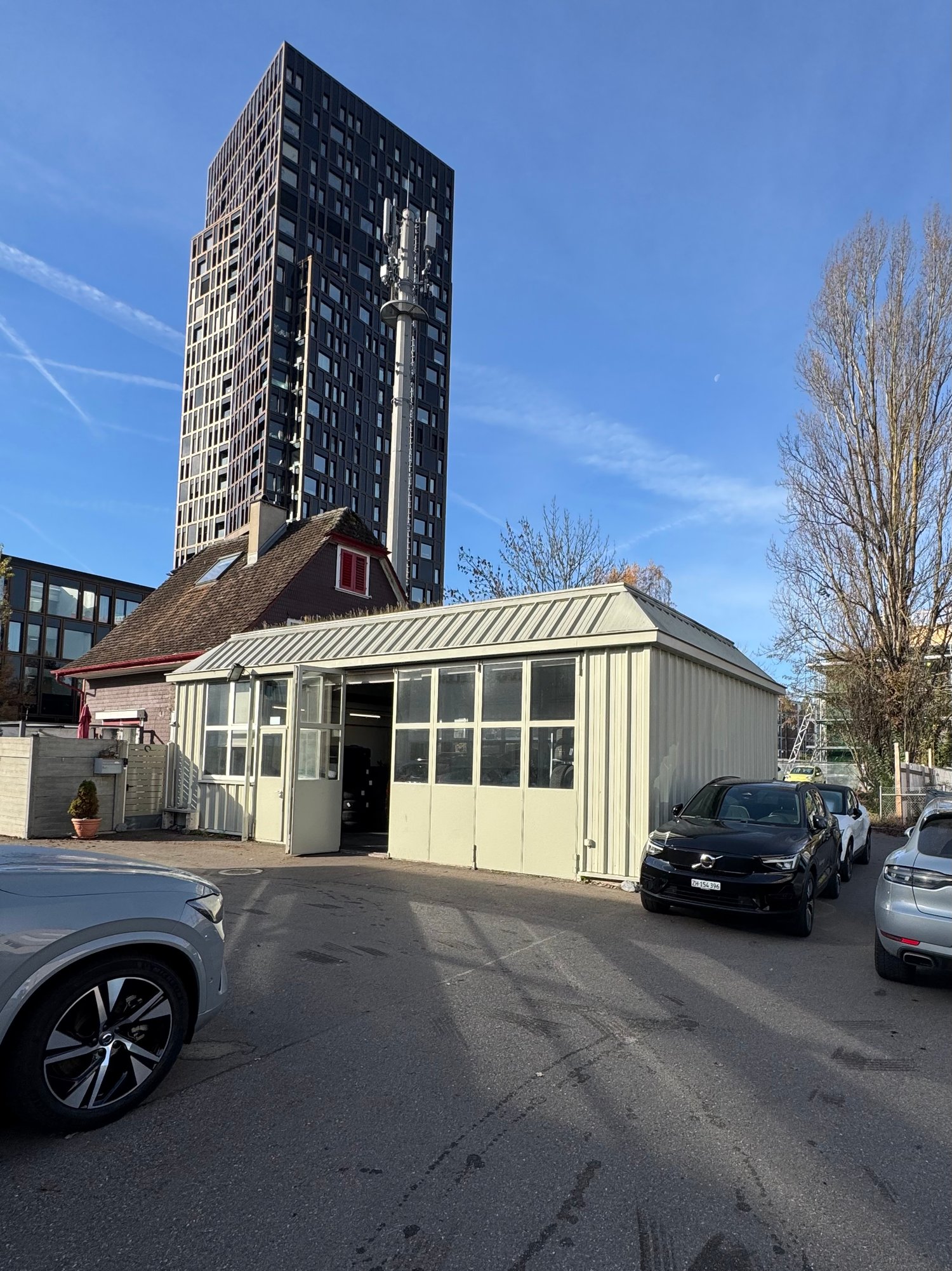 Commercial area with several cars parked in front of the building, a tall skyscraper behind, garage with multiple windows