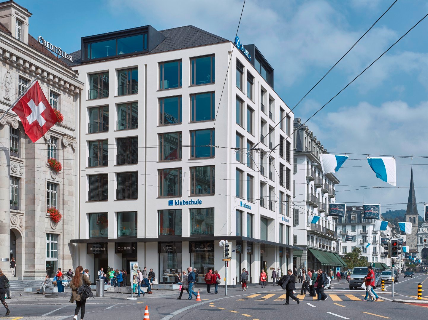 Modern white building with glass windows, multiple floors, and a blue sign reading 'Z ZURICH', located in a busy city street with people walking and streetlights.