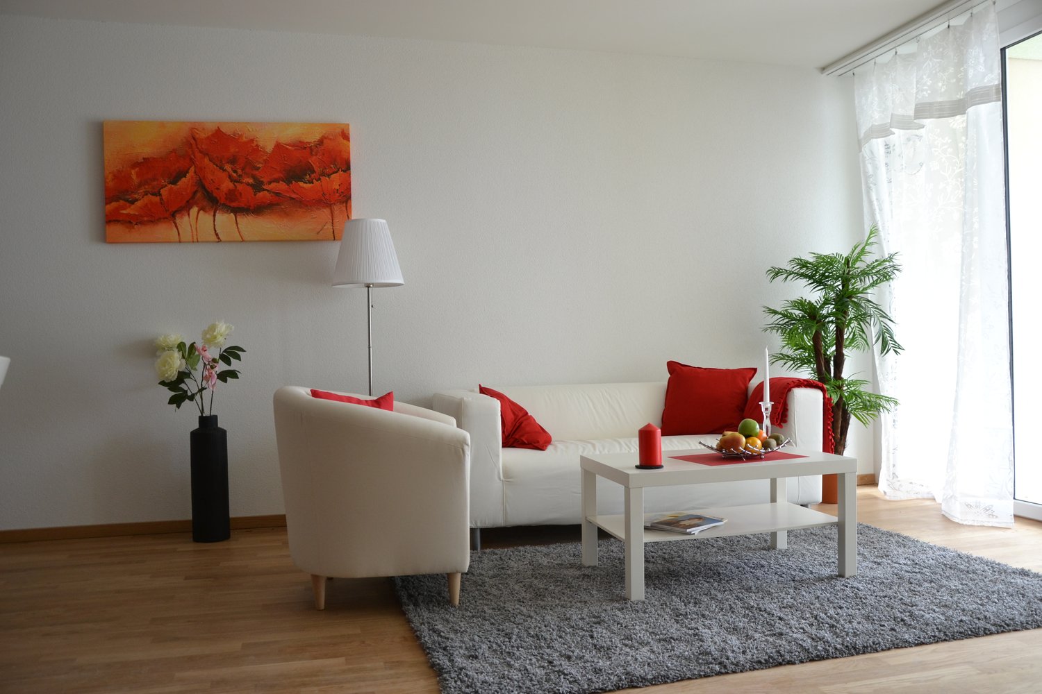Living room, white couch, red pillows, armchair, floor lamp, coffee table, decorative items, window with curtains