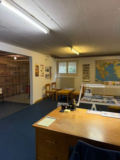 Office room with wooden desks, chairs, radiator, map on the wall, and a window.