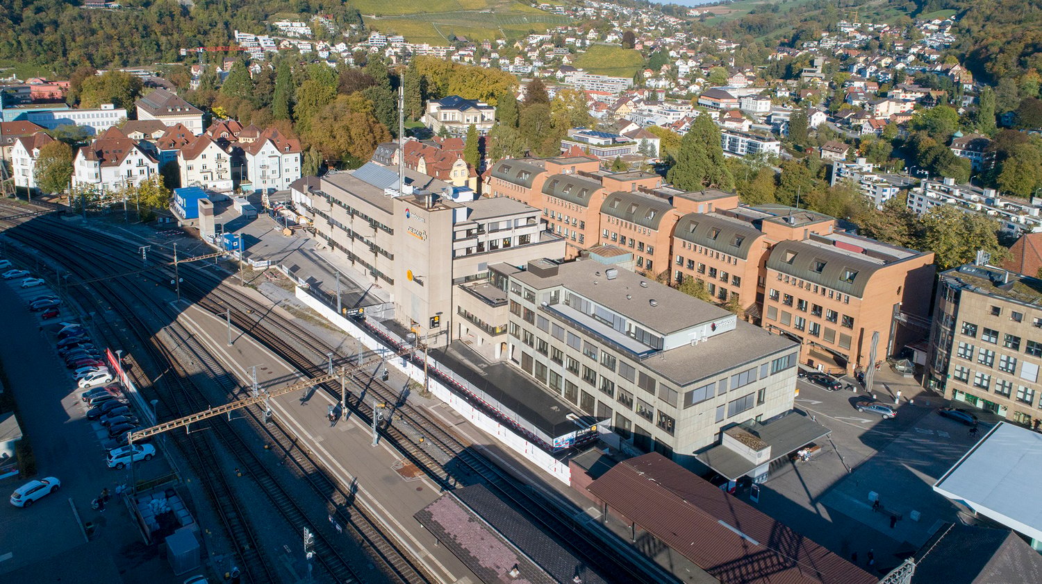 multi-story building with a slanted roof, close to the train station, several other buildings in the background