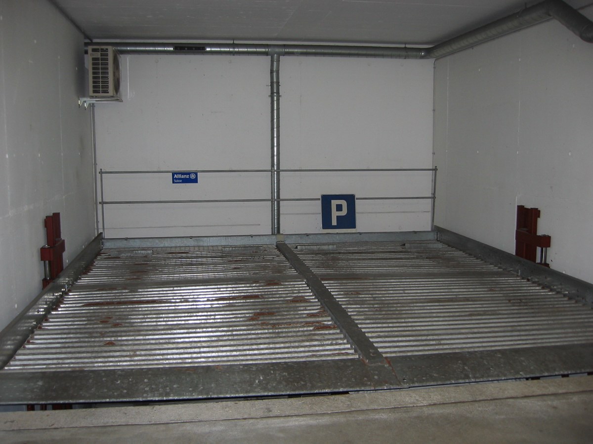 Enclosed parking space with metal racks and an Allianz sign indicating it is a parking area.