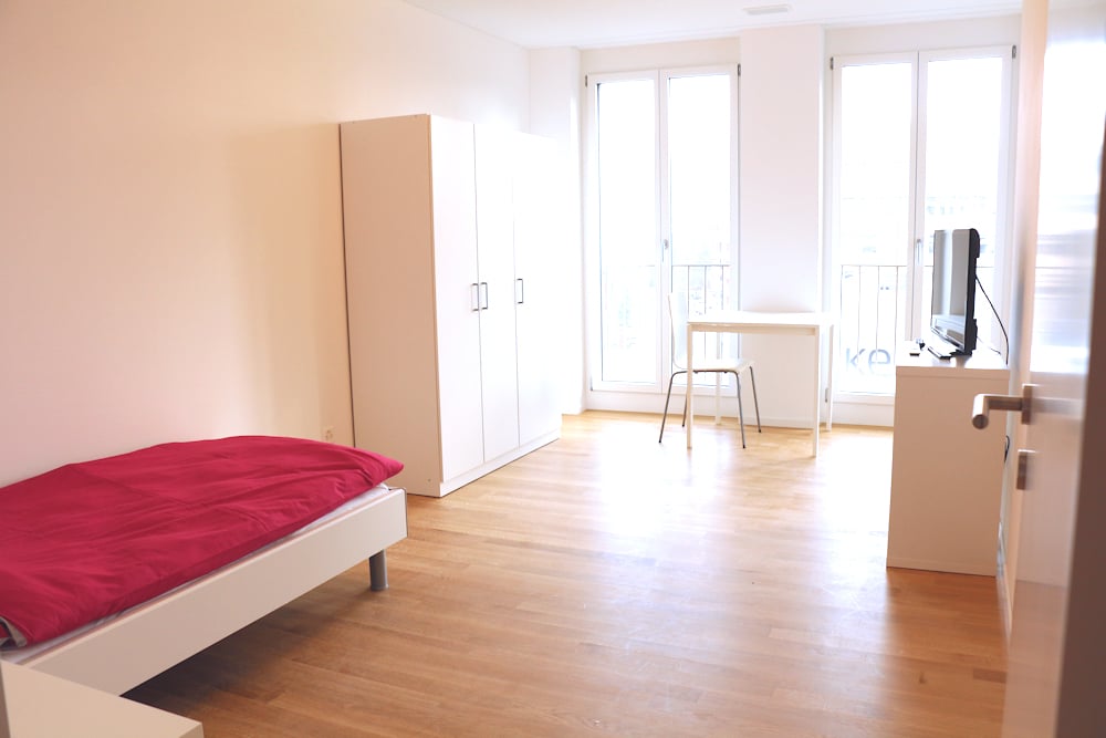 Single bed, white cabinet, desk with chair, balcony with balcony rail, television