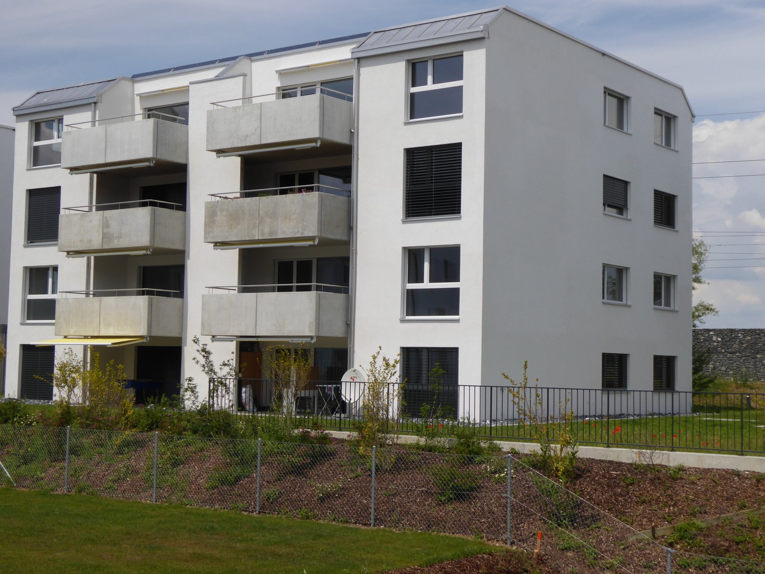 3-story apartment building with white exterior, balconies, and landscaped grounds