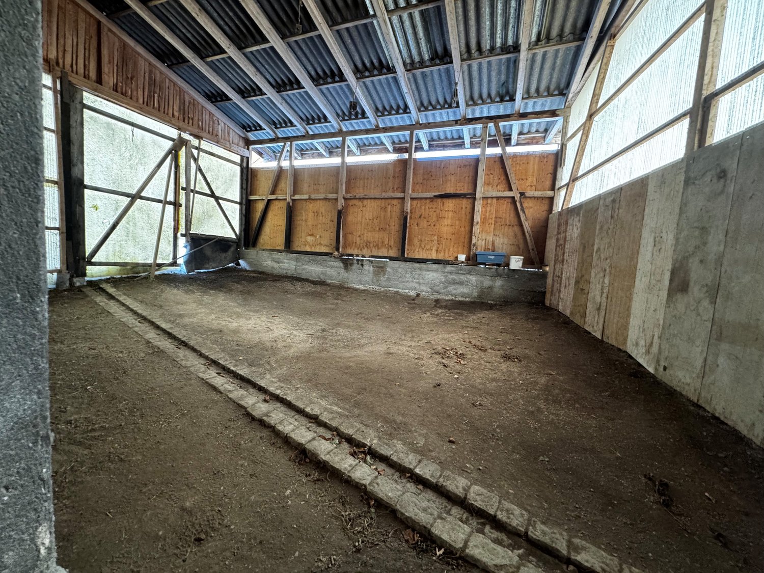 empty room, dirt floor, wooden walls, large open windows, metal roof