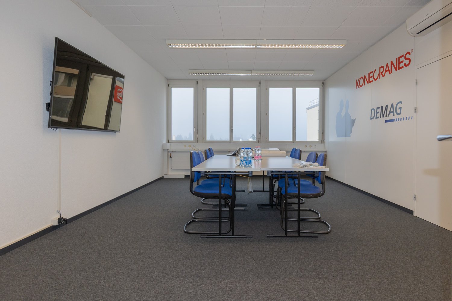 empty room, desk, chairs, flatscreen TV mounted on wall, windows, carpeted floor
