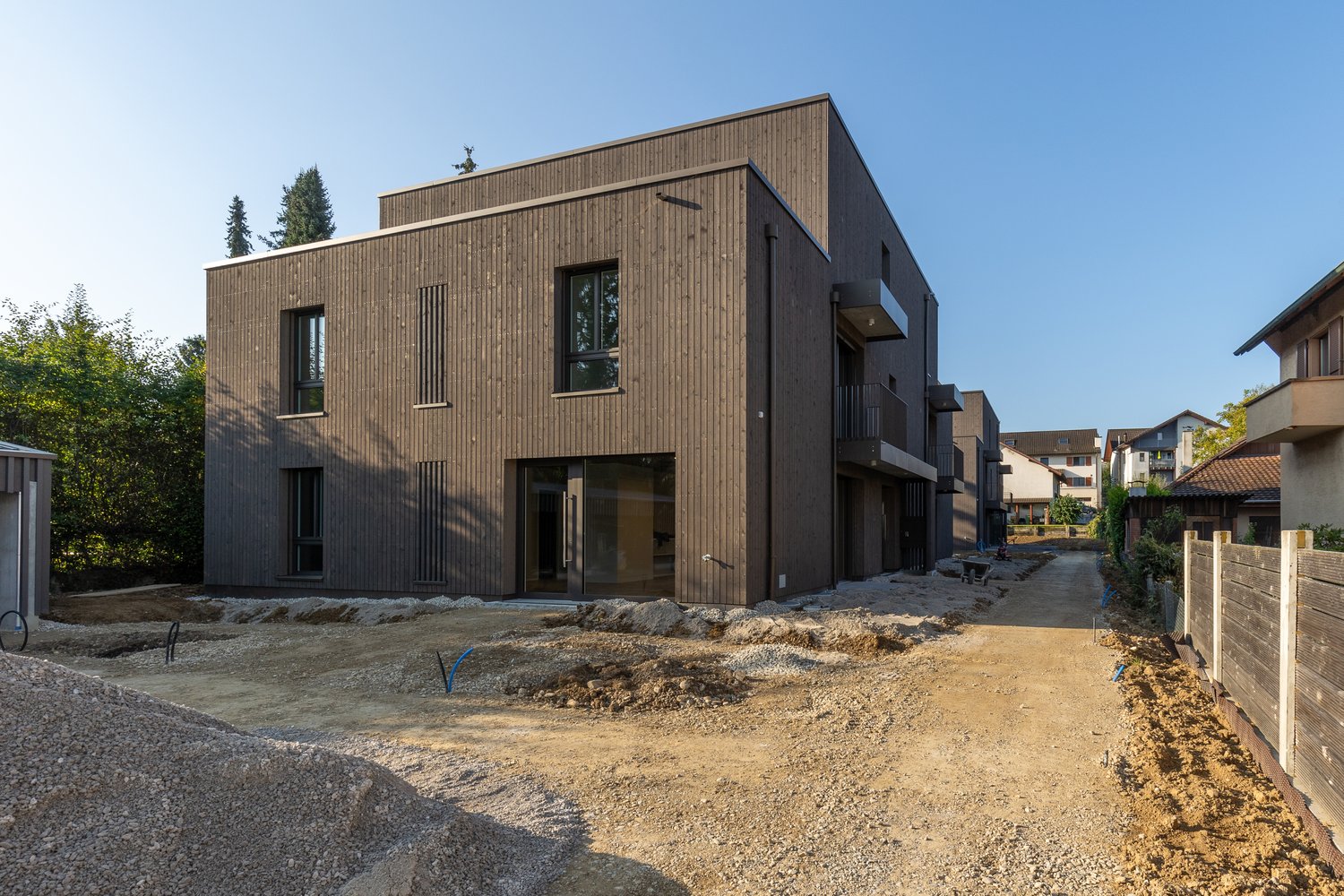 Modern house, brown wooden exterior, large windows, balcony, under construction
