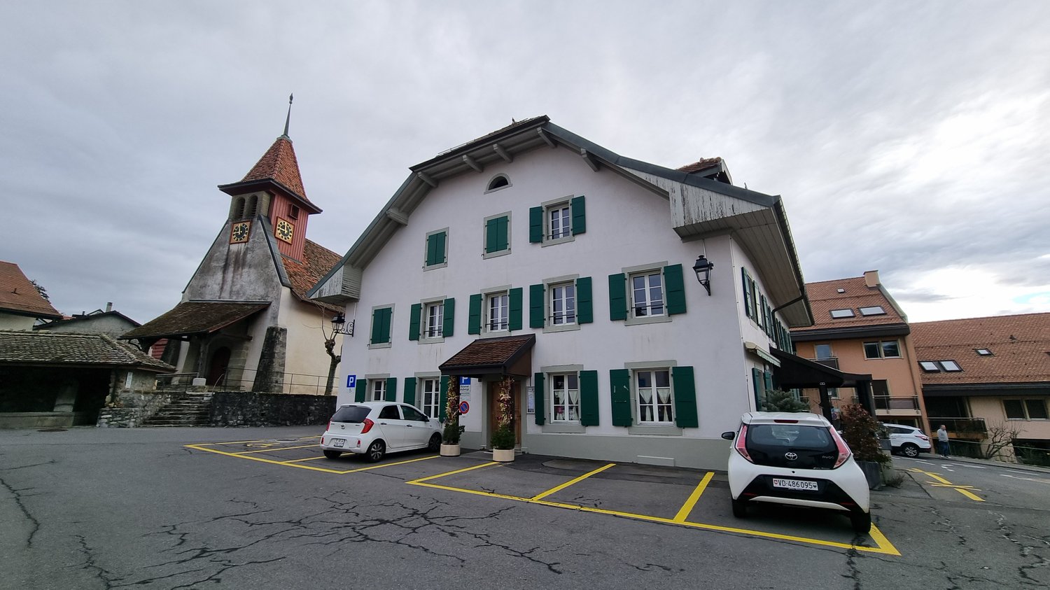 white house, green shutters, brown roof, parking lot, 2 cars parked