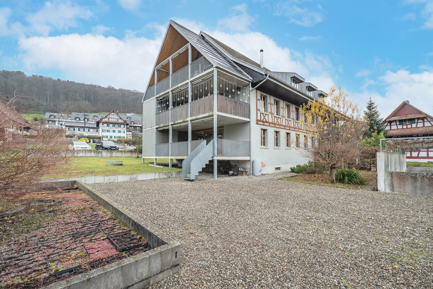 modern house, 3 stories, large balcony, metal railings, grey gravel driveway, mountain in background