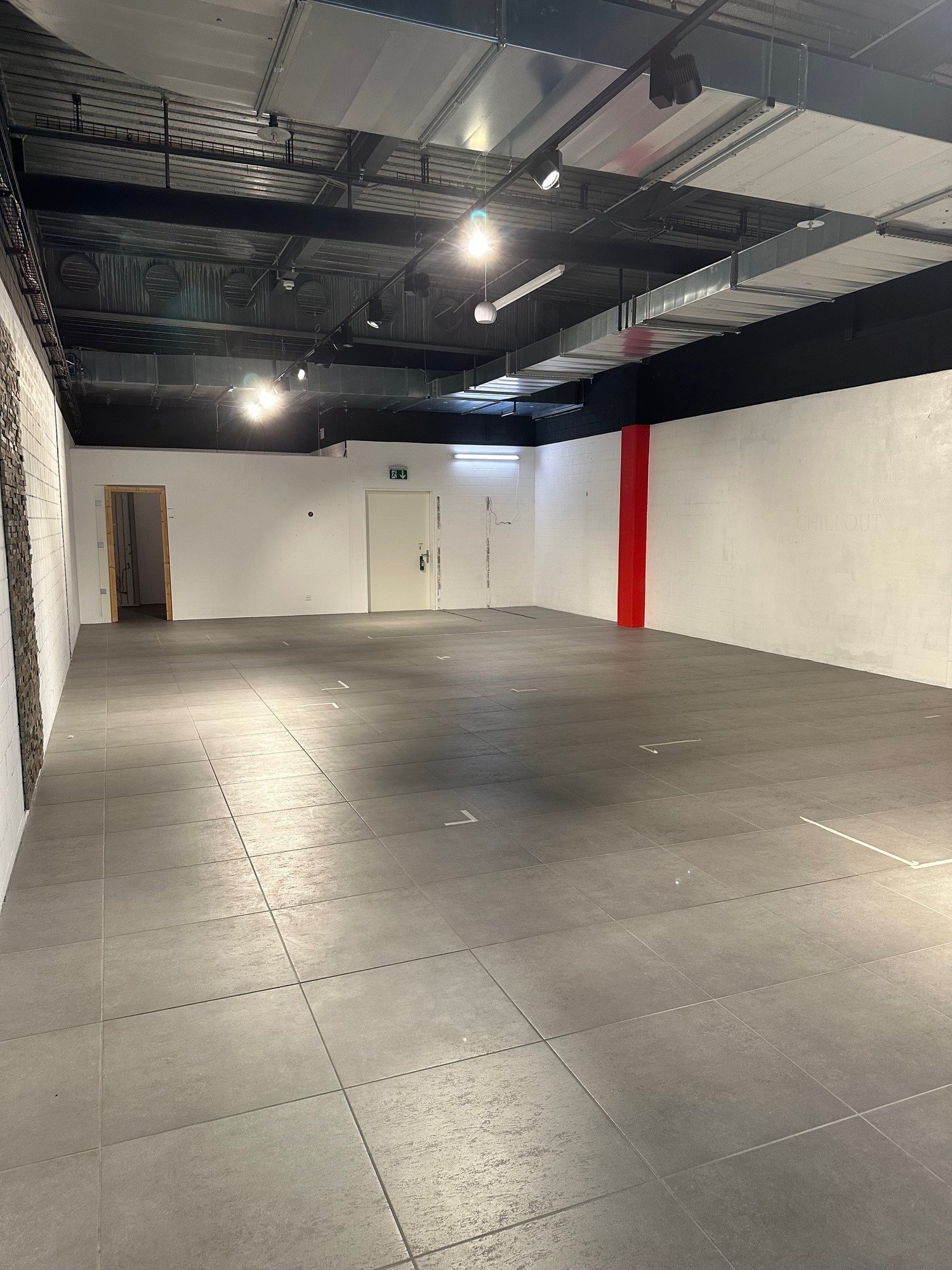 Empty room with white walls, gray floor, two doors, and a red pillar.