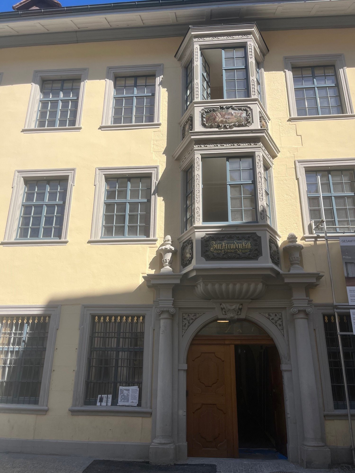 yellow building, multiple windows, wooden door, balcony with decorative elements