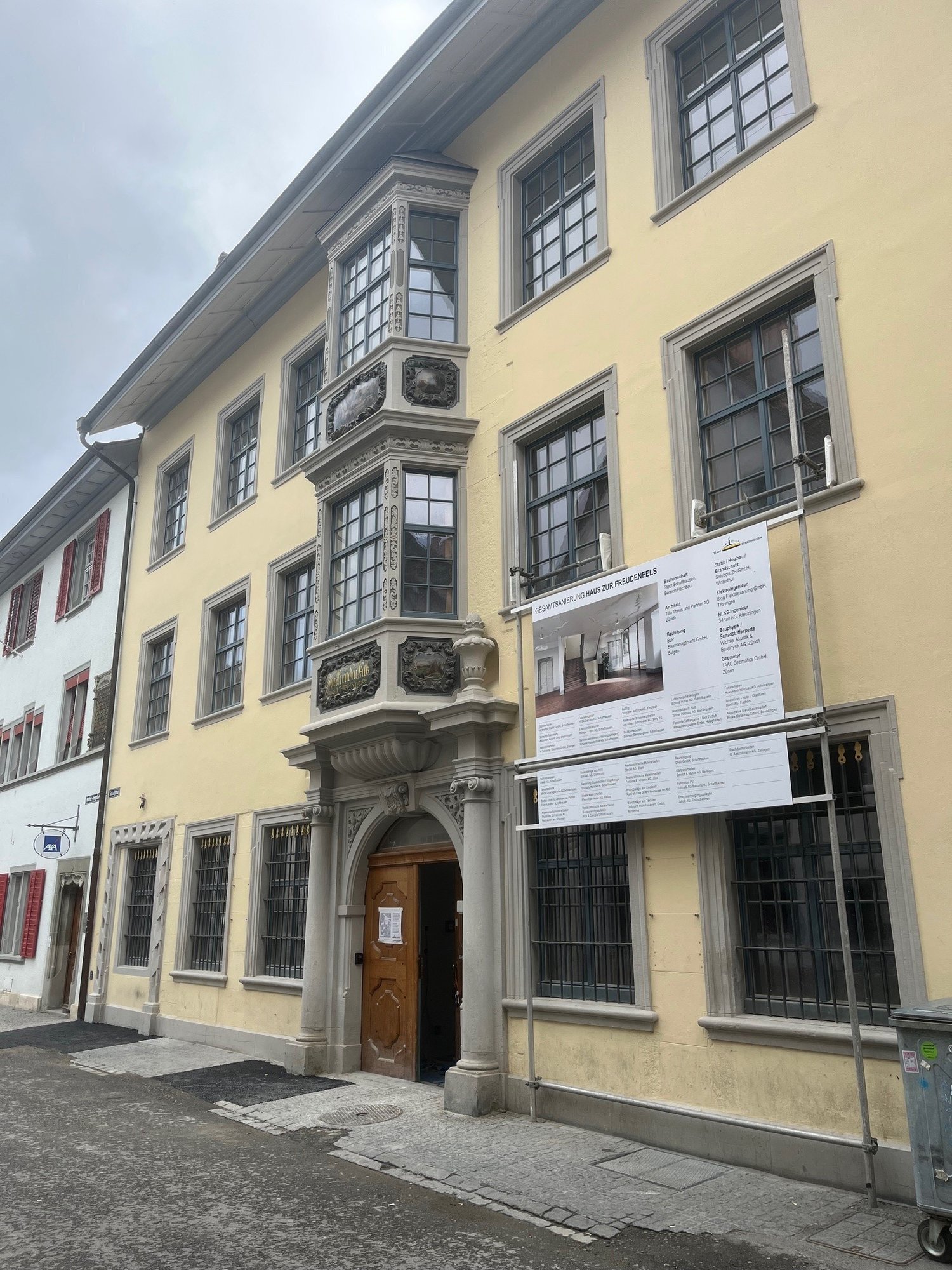 A yellow building with multiple windows and a wooden door at the bottom. The building has a few signs attached to it.