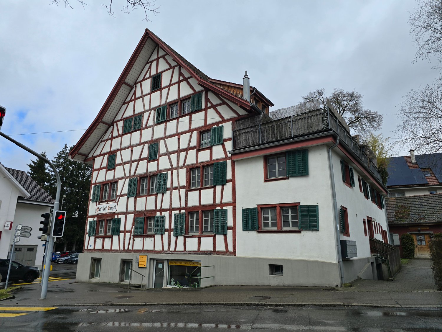 White painted, timber-framed house, red roof, multiple windows, red trims, small garden