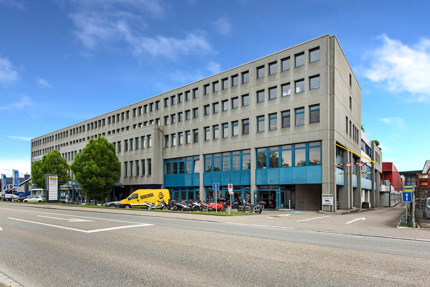 4 story office building with multiple glass windows, yellow van parked in front