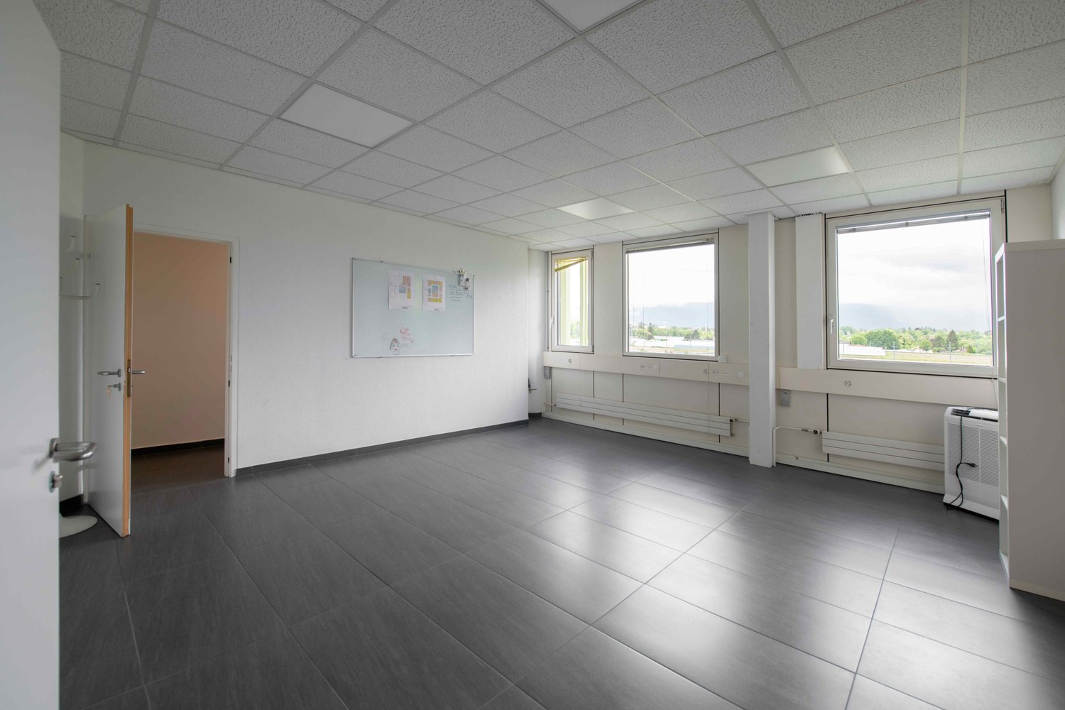 open room, large windows, whiteboard on wall, white flooring