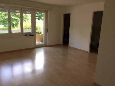 Spacious living room with hardwood floors, large windows overlooking a balcony or terrace, and neutral-colored walls.