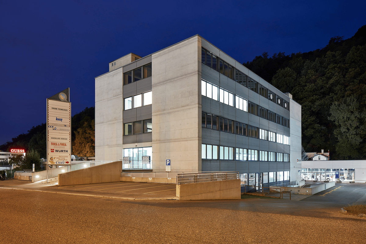 3 story office building, white walls, glass windows, front parking lot, blue signs, street light