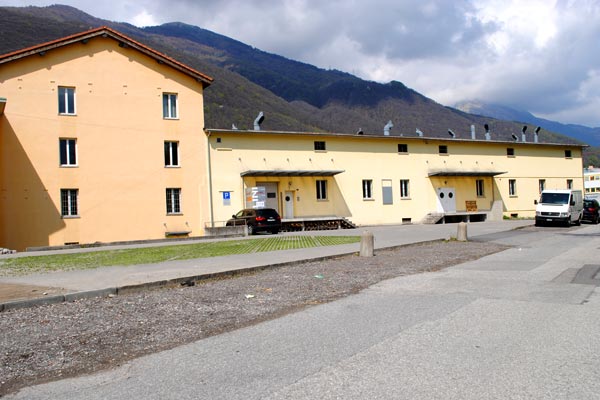 Yellow building, multiple windows, cars parked in front, mountains in the background
