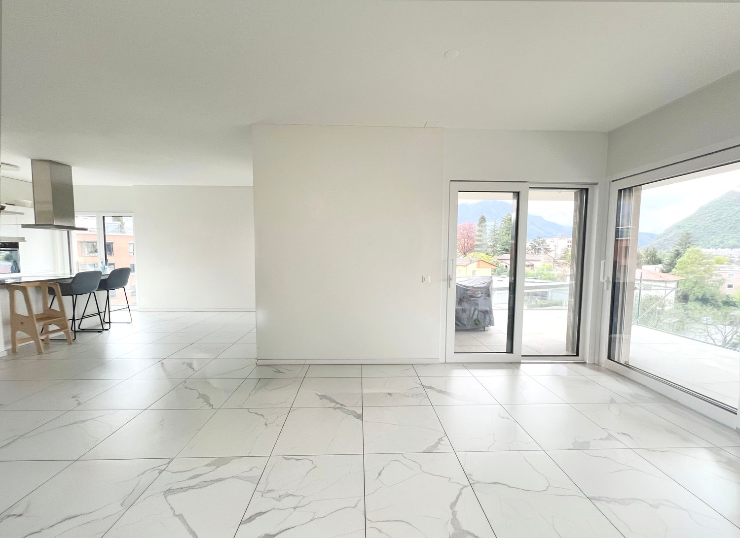 large open space, white marble flooring, white walls, large sliding glass doors, balcony, view of mountains