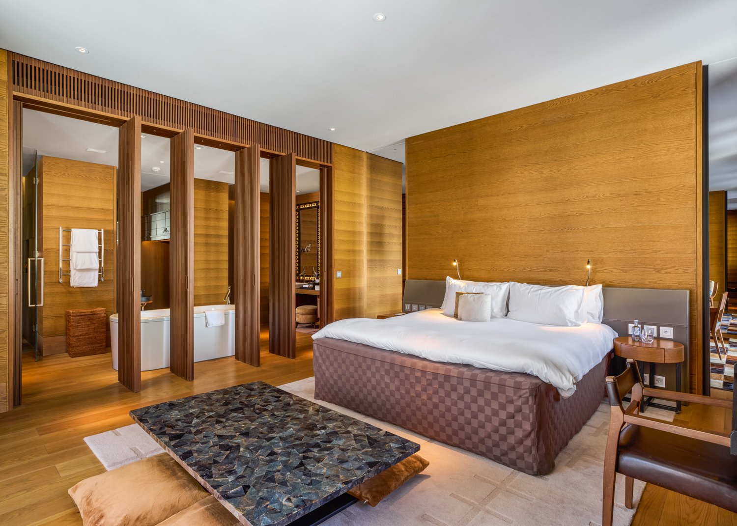 Master bedroom with wooden walls, large bed, bathtub, wooden chair, wooden table, wooden floor, white ceiling