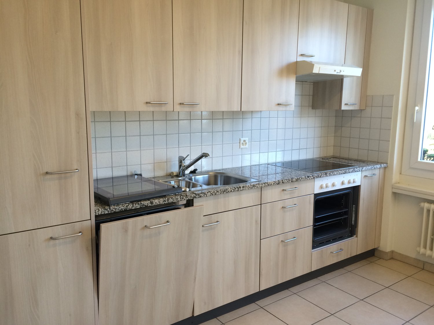 A kitchen with wooden cabinets, granite countertops, a sink, oven, dishwasher, and a window.