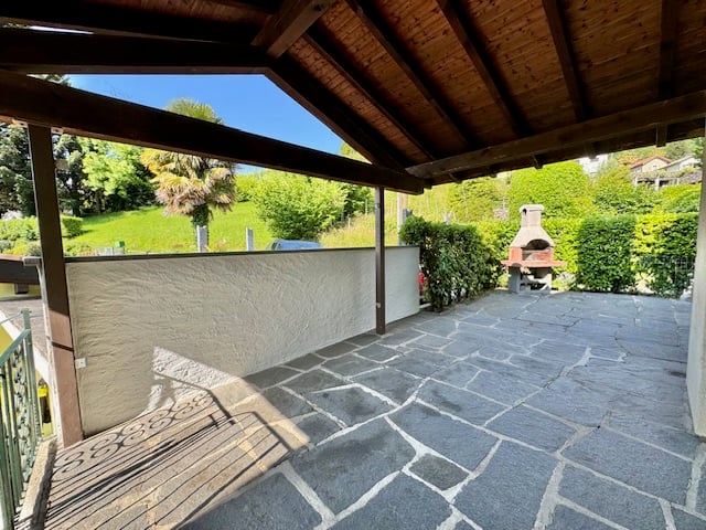 Terrace with wooden roof, fireplace, paved floor, wall, greenery, garden.