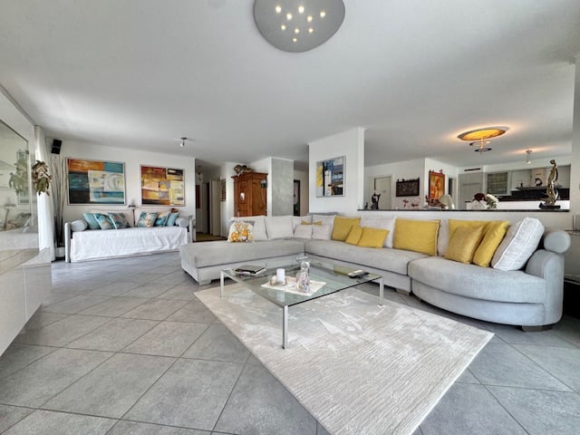 Spacious open-concept living room with large sectional sofa, glass coffee table, and artwork on the walls. The room has a modern and bright design with tile flooring and recessed lighting.