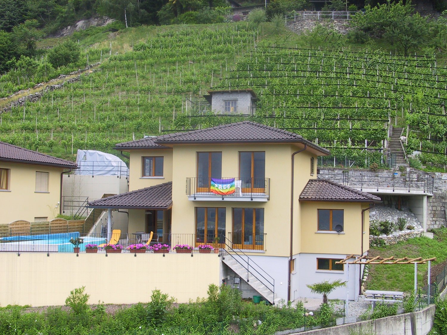 3 story house, brown roof, swimming pool, yellow walls, balcony, pool chairs, terrace, garden, vineyard view