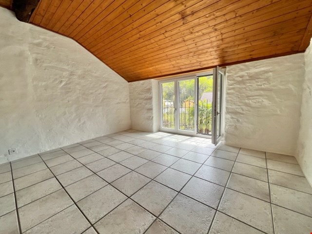A room with white tiled floor and white walls, a glass door, wooden ceiling and an electric outlet on the wall.