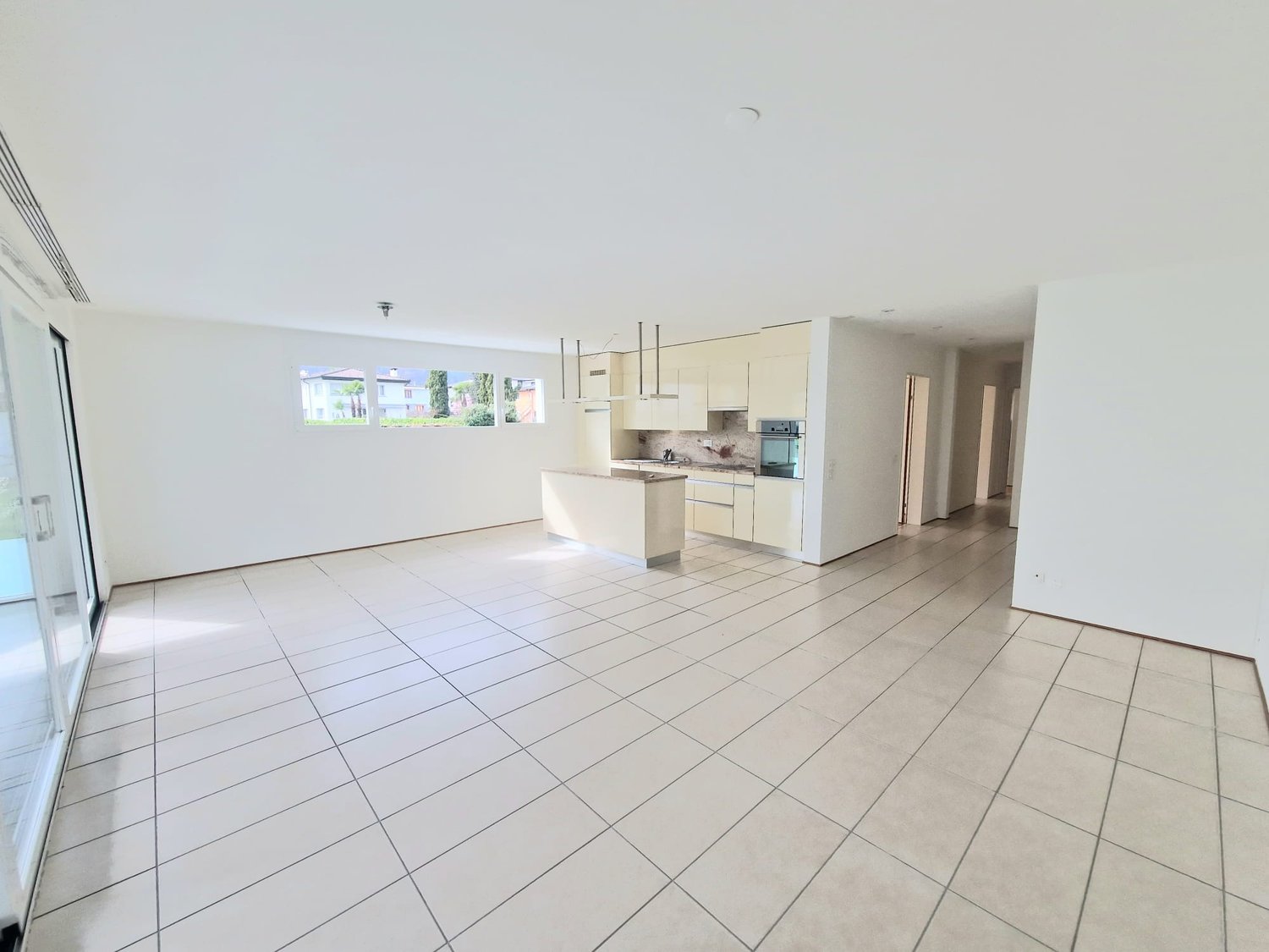 Open plan living and kitchen area, white tiles, large windows, kitchen island, modern appliances