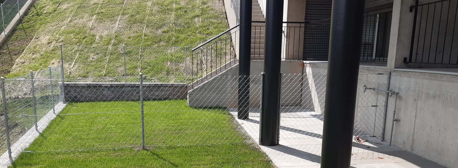 small fenced yard with short manicured lawn, stone retaining wall, black balustrade with metal railings