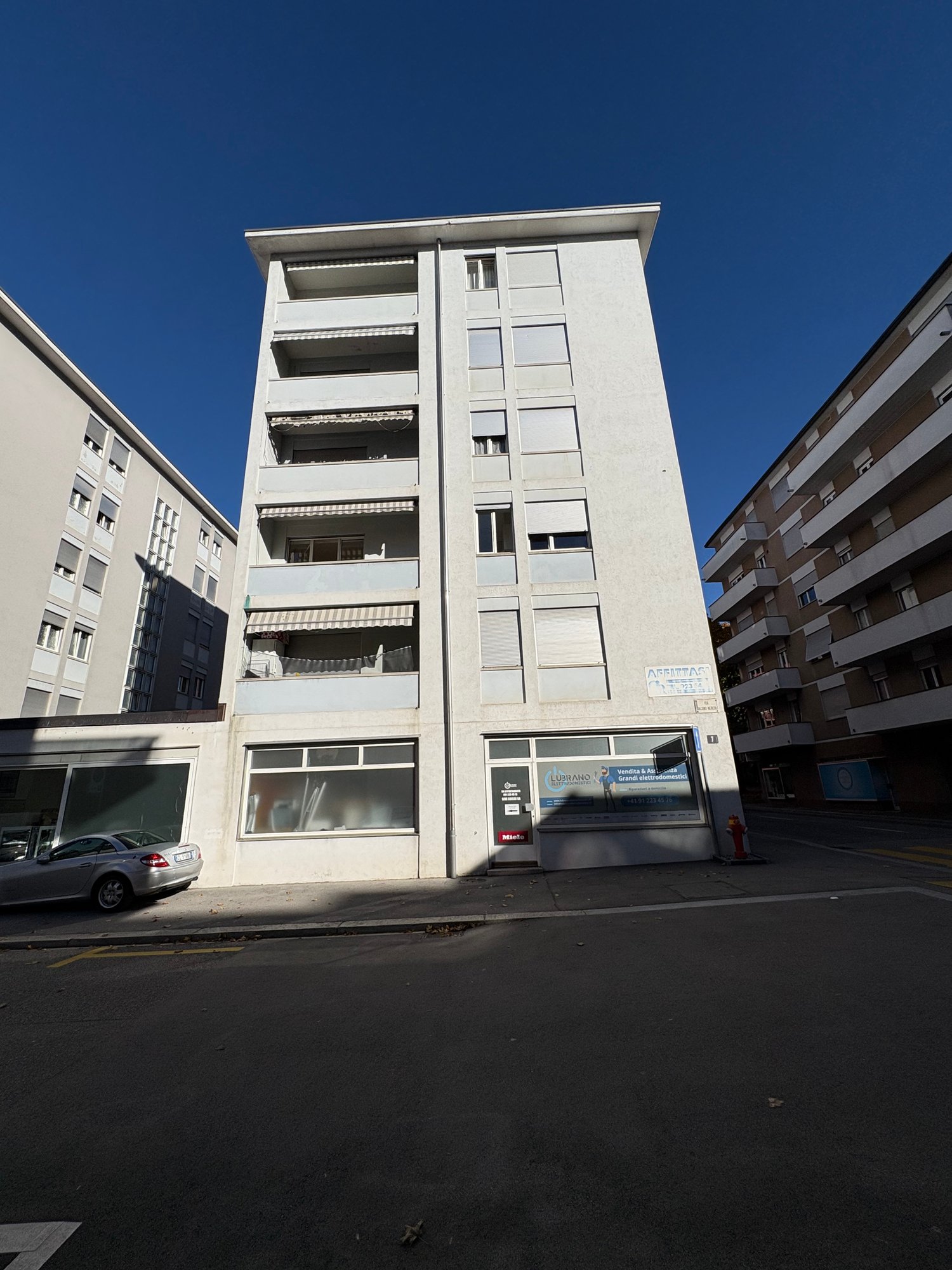 modern white building with 4 floors, balcony, car parked in front, ground floor commercial space