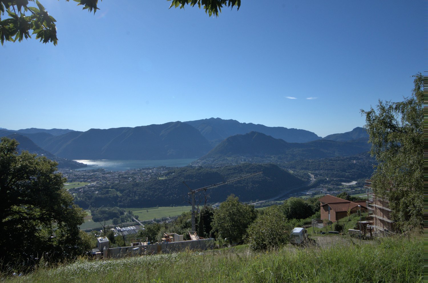 Aerial view of a scenic landscape with mountains, a lake, a town, a crane, and construction sites